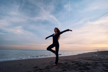 Fototapeta na wymiar woman doing a yoga practice at the beach while a beautiful sunset