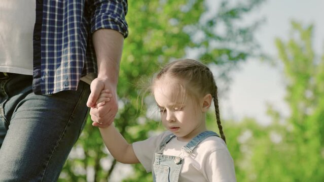 Dad and little daughter walk holding hands in the park. People in the park. Happy family walk of baby boy and father outdoors. Happy family childhood dream concept. Parents and cheerful children.