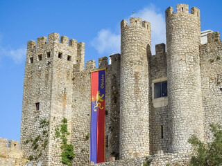 Obidos, Portugal - July 28 2019:   View of the medieval castle walls with the town flag, depcting a coat of arms of a lion with a crown