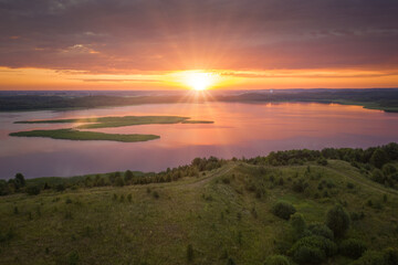 Obraz premium Amazing lake land from above, beautiful islands covered with trees and meadows in morning sunlight. Aerial, flight over Braslav Lakes National Park during fantastic sunrise. Colorful clouds on horizon