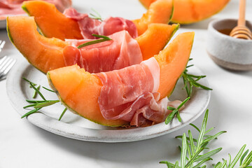 Italian antipasti. Melon cantaloupe slices with prosciutto ham, rosemary and honey in a plate on white background