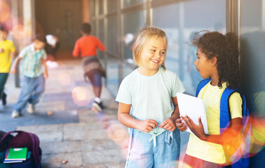Smiling tween girls friendly discussing outdoors in schoolyard during break in lessons