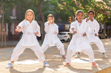 Group of schoolchildren, boys and girls, practicing karate near school outdoors