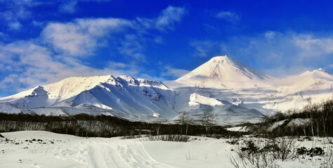 Sleeping snow-covered volcano in the rays of the setting sun. Mountain landscape with large volcano.