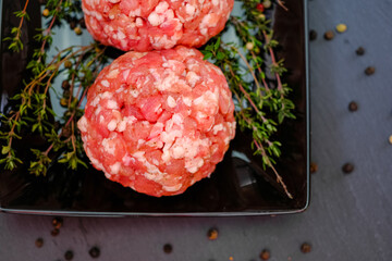 Raw minced pork.meat balls close-up. Minced meat balls with sprigs of thyme on a black plate on a...
