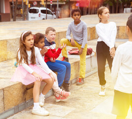 Group of smiling children sitting on stairs and chatting together sitting at urban street