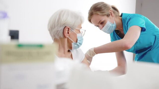 Virus prevention. Young caucasian masked nurse woman vaccinating her elderly retired patient lady in a doctor's practice. High quality 4k footage