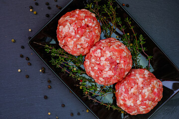 Raw minced pork.meat balls close-up. Minced meat balls row set with sprigs of thyme on a black...