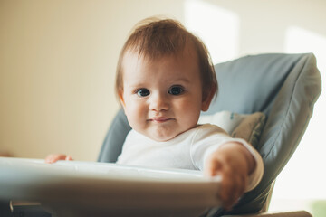 Adorable baby girl sitting in a high chair and smiling, ready for feeding. Baby care. Beautiful girl.