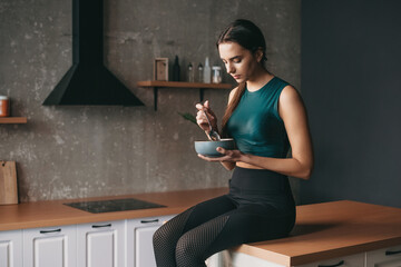Sporty woman sitting in the kitchen with a bowl and a spoon, eating. Vegetarian healthy food....