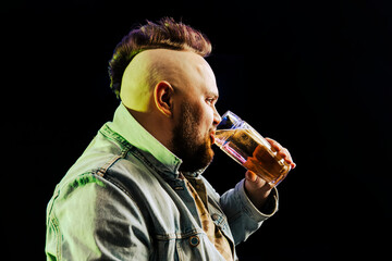 punk man with a mohawk drinks beer from a glass mug in the dark. The concept of alcohol dependence.