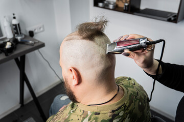 young man in a military uniform shaves his head bald for military service. A guy with a beard gets...