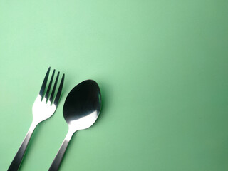 Stainless steel forks and spoons arranged on a green background..