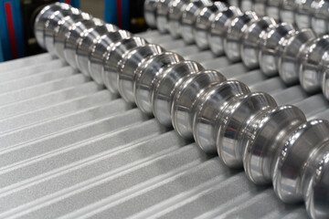 Corrugated metal roofing panel passing through roll former machine