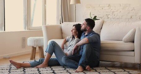 Serene loving married couple newlyweds sit on soft cozy carpet hug smile hold romantic conversation plan to buy new family house. Smiling millennial lovers relax dream of happy future life together