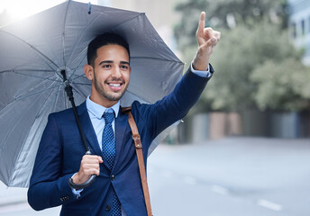Taxi. Cropped shot of a handsome young businessman with an umbrella hailing a cab while on his...
