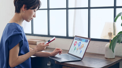 おしゃれなオフィスでパソコンとスマホを使う女性