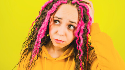 Young woman with thoughtful look on yellow background. Beautiful female with curly hair looking up, scratching head and reflecting on life.