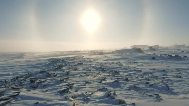 Bright SOLAR HALO forms around SUN in clear SKY above frozen ARCTIC LANDSCAPE covered with SNOW.