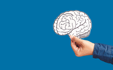 Close-up of hand holding a brain shape made from paper over a blue background
