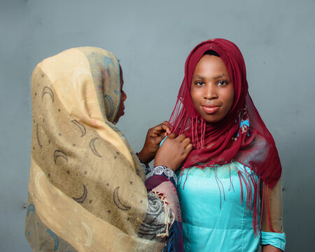 Two African Nigerian Female Muslim Sisters Or Friends With One Helping The Other Out With Her Hijab Scarf During Ramadan