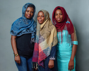 Three African Nigerian female muslim sisters or friends with Hijab scarf, standing curdled together...