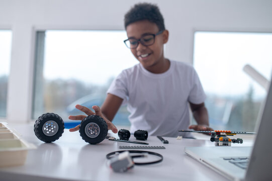 A cute teen sitting at the table and playing with toy wheels