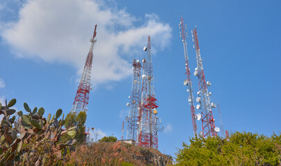communication towers on top of a mountain in the middle of the desert forest, blue sky in summer day, rocks and palms