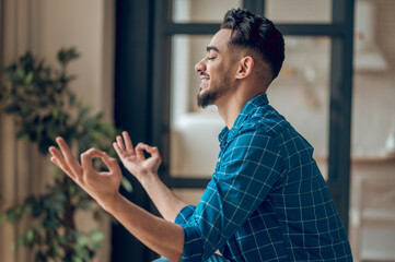 Positive young yogi sitting in lotus pose with fingers in giana mudra