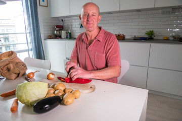 A man peels vegetables - potatoes, carrots, peppers, cabbage- at the kitchen table.