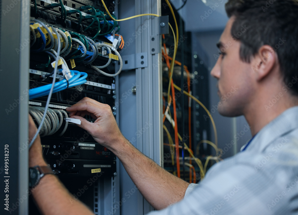 Poster Lets get technical. Cropped shot of a handsome young male programmer working in a server room.