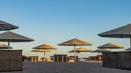 A beach on the Red Sea coast. Latticed sun umbrellas, ceramic urns and wicker fences stand on the sand. Clear blue sky. Light and shadows. Egypt. Safaga.