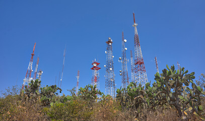 communication towers on top of a mountain in the middle of the desert forest, blue sky in summer day, rocks and palms