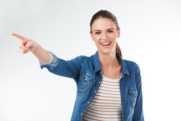 Direct your eyes over there. Studio portrait of a young woman pointing against a grey background.