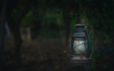 Fototapeta na wymiar Rusty old lantern hangs in the forest, vintage lamp in dark tone