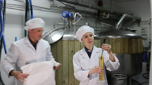 Man and woman brewmasters measuring strengh of beer sample with alcoholometer.