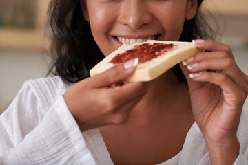 Woman biting sandwich with berry jam she made for breakfast