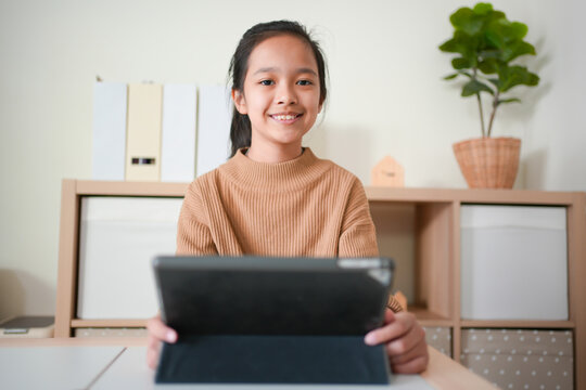 Asian kid studying online using tablet in a living room alone.