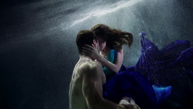 tenderness and passion of lovers floating underwater, young woman and handsome man are embracing