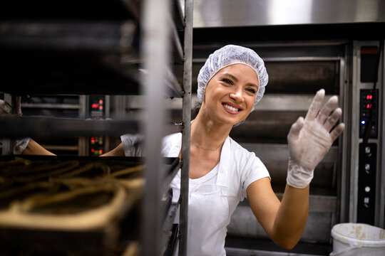 Portrait of female baker in white clean uniform and hairnet moving trays with bread in bakery production.