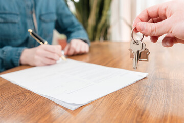Close up of female client's hands signs the contract. Realtor gives the keys to the woman. The concept of insurance, mortgage and rental of real estate
