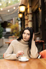 Portrait of a joyful young woman enjoying a cup of coffee in a cafe. Smiling beautiful girl drinking hot drink in autumn.