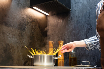 Close-up. A woman in an apron cooks spaghetti in the kitchen.