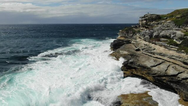 Rocky coast near Bondi beach with stormy waves crashing on cliff in Australia. Aerial