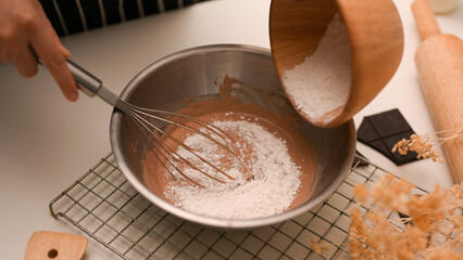 Female preparing a cookies dough, adding a cup of flour into a mixing bowl