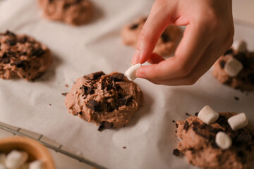 Female hands adding some marshmallow on a chocolate cookies dough.