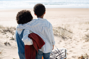 Back view of African American children on beach. Brother and sister in casual clothes looking at water, hugging. Portrait, family, childhood concept