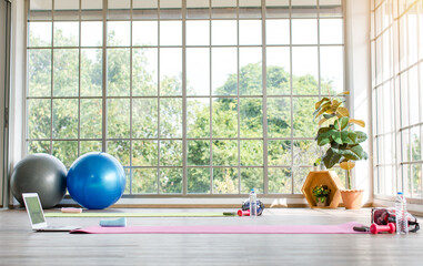 Interior glasses windows garden view indoor workout sport yoga pilates activity classroom with equipment, mat, exercise balls, dumbbells, water bottles and laptop notebook computer for online lesson