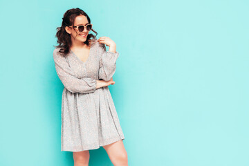 Young beautiful smiling female in trendy summer dress. Sexy carefree woman posing near blue wall in studio. Positive model having fun. Cheerful and happy. In sunglasses