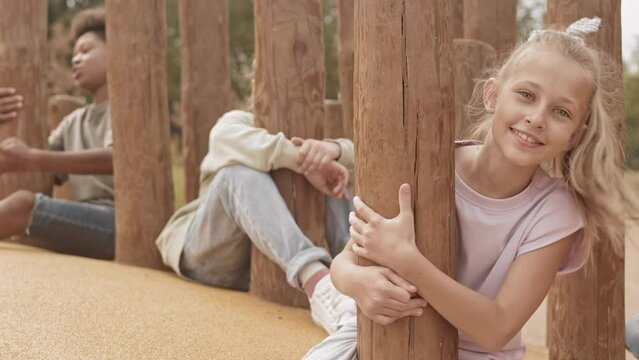 Slowmo portrait of pretty 10 year old Caucasian girl and her multiethnic friends smiling and waving at camera playing together on playground